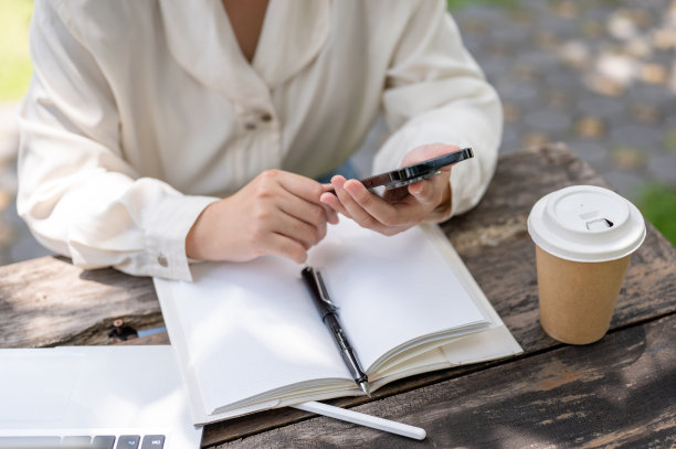 一名女子在花园的桌子旁工作时使用智能手机的图片。图片下载