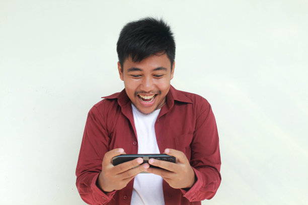 年轻的亚洲男子在玩手机游戏时的微笑和快乐的脸。图片下载