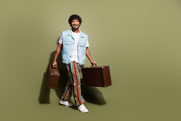 有魅力的年轻人的全身照片，手持复古的手提箱，穿着时尚的牛仔衣服，在卡其色背景上孤立图片下载