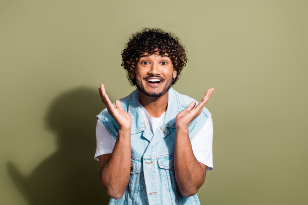 漂亮的年轻男性的照片肖像惊讶地举手穿着时尚的牛仔服装孤立的卡其色背景图片下载