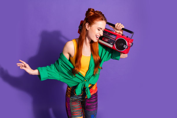 照片的好心情华丽的红头发的女孩穿着绿色的衬衫拿着复古音箱在肩上跳舞孤立的紫罗兰色背景图片下载