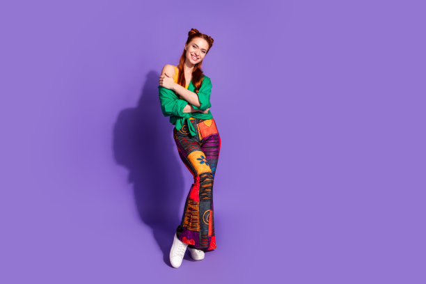 华丽可爱的女孩全身照片穿着绿色衬衫时尚的印花裤子拥抱自己孤立的紫罗兰色背景图片下载