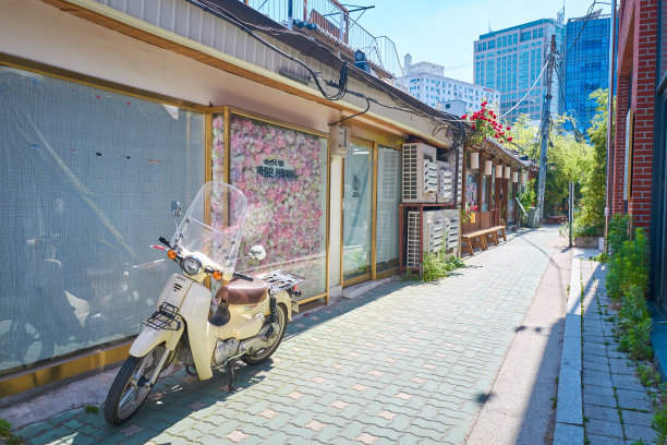 韩国首尔，白色摩托车停在有商店和花卉装饰的狭窄街道上图片下载