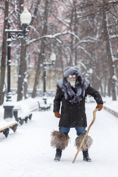 一位头发花白、留着漂亮胡子的老人望向远方，微笑着。一个上了年纪、头戴皮草帽、身穿皮草大衣的时尚潮人的特写。圣诞节图片下载