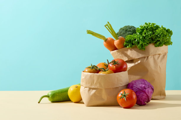 蓝色背景下的正面角照片，黄色台面上的两个纸袋里装着新鲜蔬菜。左侧空白，用于展示产品图片下载
