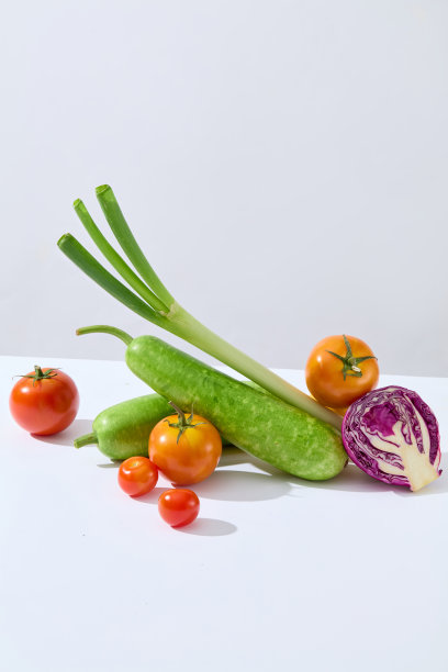在浅灰色的背景下，白色的台面中央摆放着新鲜的有机蔬菜，包括绿色的南瓜、韭菜、西红柿和紫色的卷心菜。素食烹饪产品宣传照片图片下载