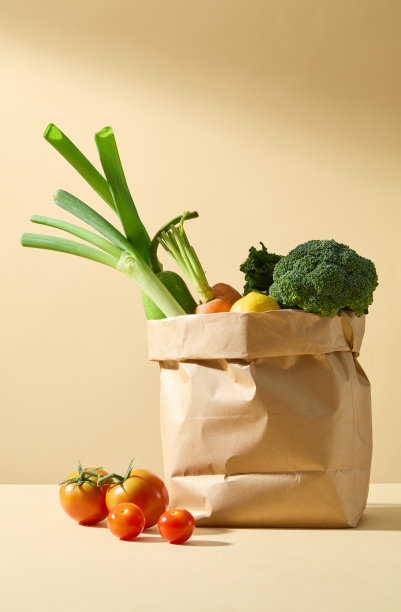 黄色的桌面上放着一个超市纸袋，里面装着烹饪用的素食原料，旁边是一些成熟的西红柿。烹饪产品广告照片图片下载