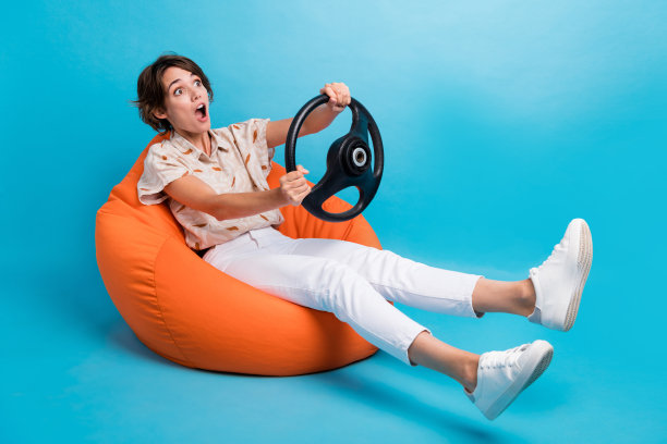 疯狂震惊的女孩坐在豆袋驾驶汽车快速冒险的照片看起来空旷的空间孤立在蓝色的背景图片下载