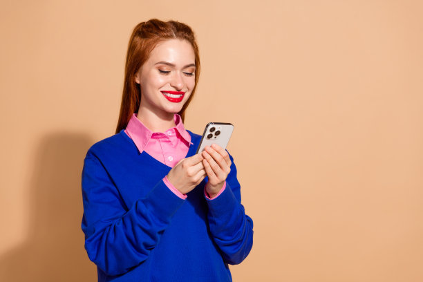 照片中迷人迷人的女士穿着蓝色套头衫聊天苹果iphone手机空空间孤立米色背景图片下载