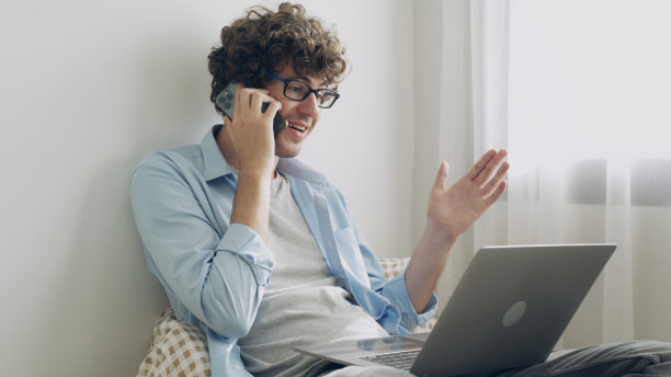 年轻的商人或自由职业者正在使用电脑笔记本电脑，思考他的业务想法，并在电话中谈论他的工作。图片下载