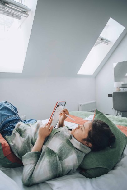 年轻的亚洲女子舒适地躺在床上，全神贯注地在平板电脑上创作数字艺术图片下载