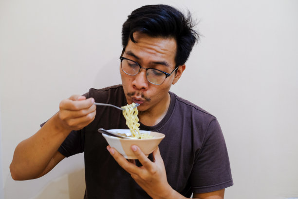 一名东南亚男子拿着白碗里的面条吃图片下载