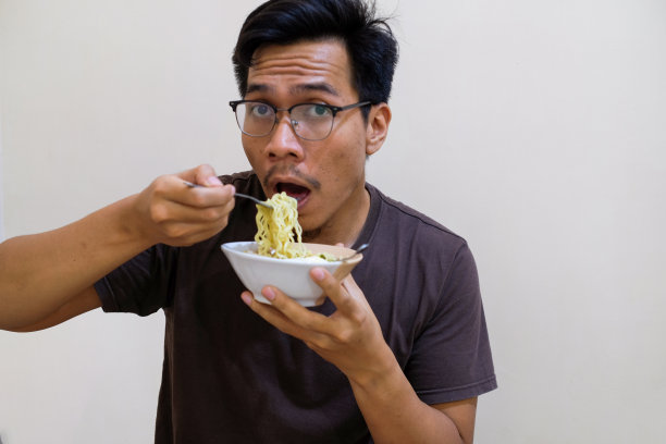 一名东南亚男子拿着白碗里的面条吃图片下载