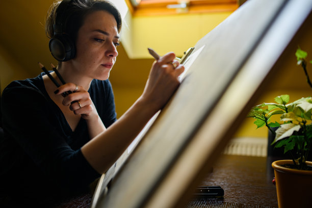 专注的艺术家与耳机在绘图板上铅笔绘图。图片下载
