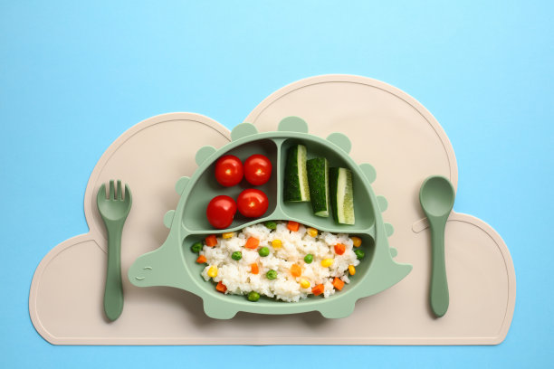 健康的儿童餐放在一个有趣的恐龙形状的盘子里，背景是蓝色的图片下载
