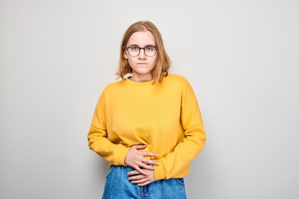 患有胃痛的女学生肖像被隔离在白色的摄影棚背景上。肠胃问题的概念图片下载