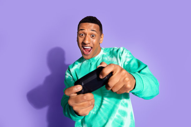 照片中的开朗积极的家伙穿着绿松石运动衫享受playstation游戏的空旷空间孤立的紫罗兰色背景图片下载