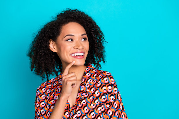 照片中梦幻的少女女士穿着印花衬衫，手指下巴看起来空白，孤立的蓝色背景图片下载