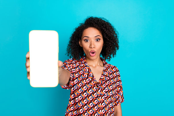 无语的女人穿着衬衫的照片展示你的促销智能手机显示惊讶地盯着孤立的蓝色背景图片下载
