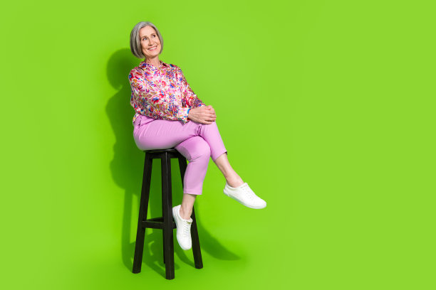 梦幻般的漂亮女士的全身照片，穿着粉红色的衬衫，坐在凳子上，看着空旷的空间，孤立的绿色背景图片下载