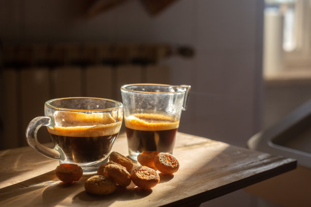 两杯透明的意大利浓缩咖啡，木质表面上有小饼干。高对比度的早晨厨房照片。背景模糊。夫妻自制早餐。壁纸图片图片下载