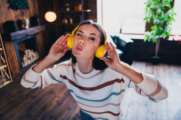 可爱的年轻女子跳舞的照片听音乐耳机空气亲吻眨眼穿条纹装室内家庭客厅在棕色暖色图片下载