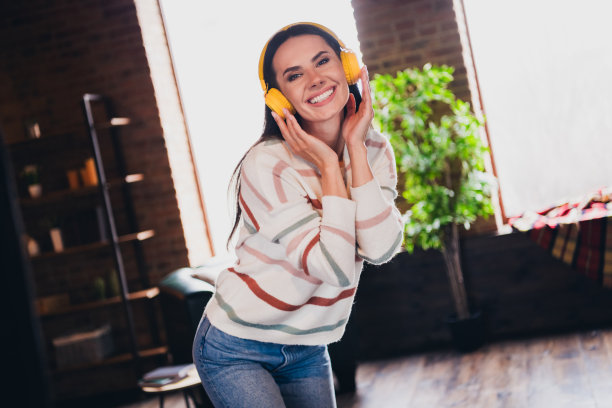 可爱的年轻女子跳舞的照片，听音乐，耳机，穿着条纹装室内的家庭客厅在棕色暖色图片下载