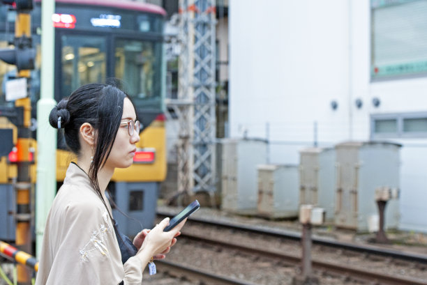在日本大阪伏见稻荷神社车站，等待铁路道口的持手机的男人图片下载