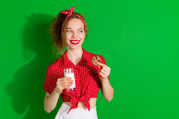 照片肖像可爱的年轻女士看起来空的空间牛奶玻璃饼干穿着时尚的红色复古服装孤立在绿色的背景图片下载