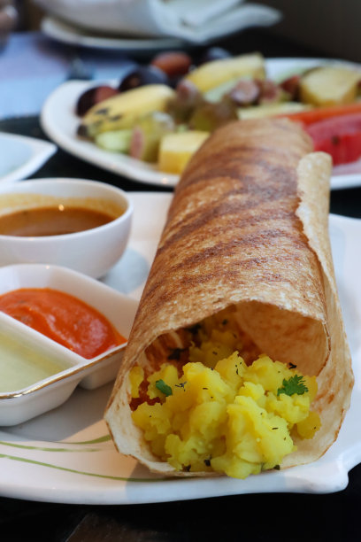 特写图片，盘子里有印度dosa美味煎饼，可丽饼里塞满了masala土豆泥和切碎的洋葱，配上椰子酸辣酱和桑巴，水果沙拉，酒店餐厅的餐桌设置，重点放在前景上图片下载