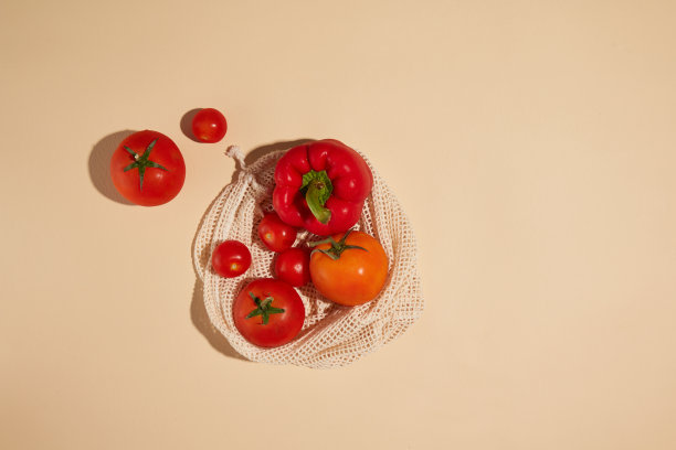 创意照片高角度拍摄的红色蔬菜组成，红色的甜椒和成熟的番茄在白色网袋，放在黄色的台面。设计及广告位图片下载