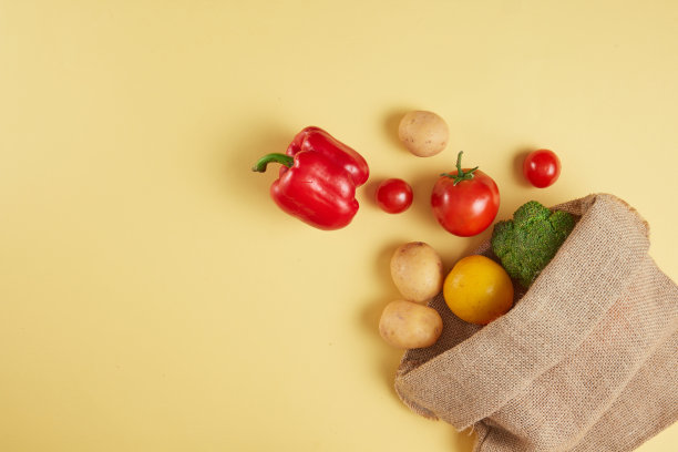 创意模板，在黄色背景上的新鲜蔬菜，用棕色帆布袋装饰。图片用于俯视图的宣传，左侧为产品展示留出空间图片下载