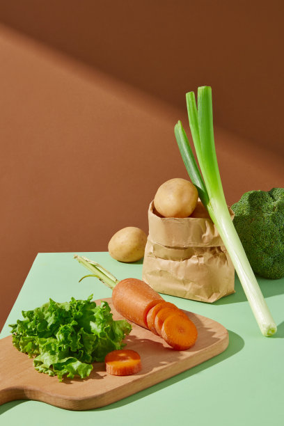 高角度拍摄的棕色背景照片，绿色的台面上有一个装着生菜和胡萝卜的木托盘，背后装饰着一袋土豆、一棵韭菜和一棵西兰花。文本空白图片下载