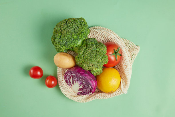 白色的网袋里有很多蔬菜，放在绿色的台面中央，旁边是一些成熟的小番茄。照片从上面的观点与空白的空间设计和广告图片下载