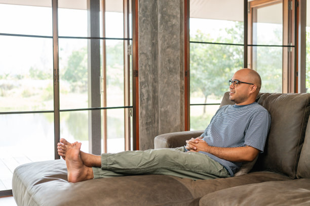 英俊的亚洲男人坐在家里客厅的沙发上休息。快乐的肖像快乐的微笑亚洲人放松在房子里。人们珍惜时间，在生活中获得成功图片下载