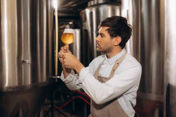 啤酒厂工人在看装在玻璃杯里的新酿啤酒图片下载