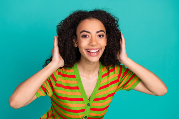 漂亮的年轻女孩的照片肖像触摸头发微笑穿着时髦的条纹服装孤立的海蓝宝石色背景图片下载