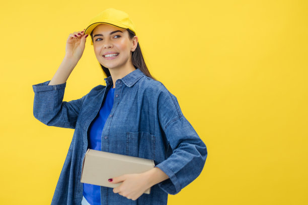 快乐的女人微笑着，拿着包裹包裹盒子孤立在黄色背景上，快递和航运的服务理念。图片下载