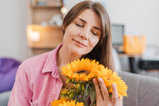 微笑的女子闭着眼睛捧着一束花，向日葵坐在沙发上图片下载