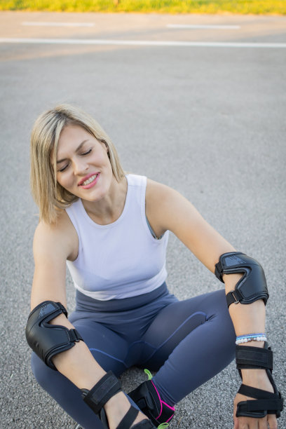 一张漂亮的金发女人穿着直排轮滑坐在路上的照片。日落时分穿着运动服的迷人女运动员。图片下载