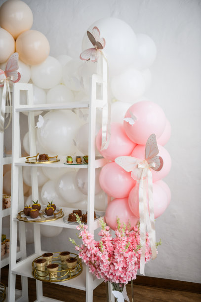在背景照片墙上为女婴准备的糖果棒和甜点。纸粉装饰蝴蝶特写。拱门装饰白色，橙色气球为生日快乐。儿童照相区。图片下载