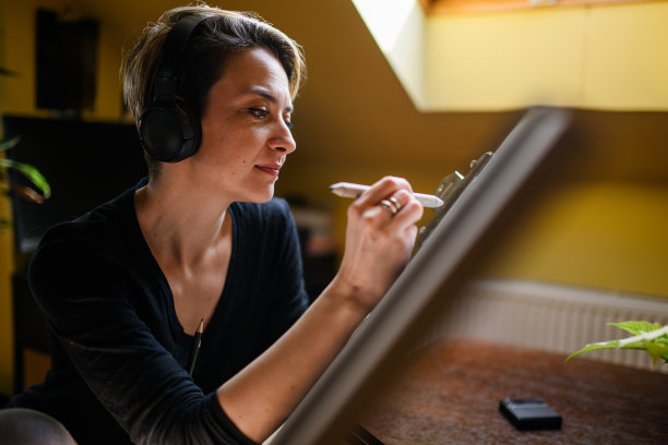 艺术家带着耳机在家里的画板上素描的侧视图图片下载