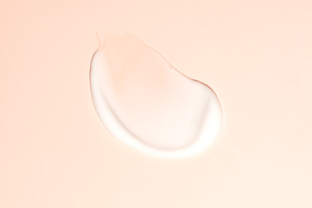 米色背景上飘逸的奶油。涂抹了流动的面霜。图片下载