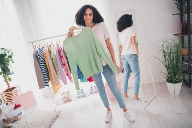 照片中可爱漂亮的女孩双手捧着时髦的服装集合装在室内试衣间衣柜里图片下载