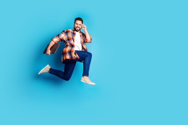 漂亮的年轻人笔记本电脑的全尺寸照片跑跳穿衬衫孤立的蓝色背景图片下载