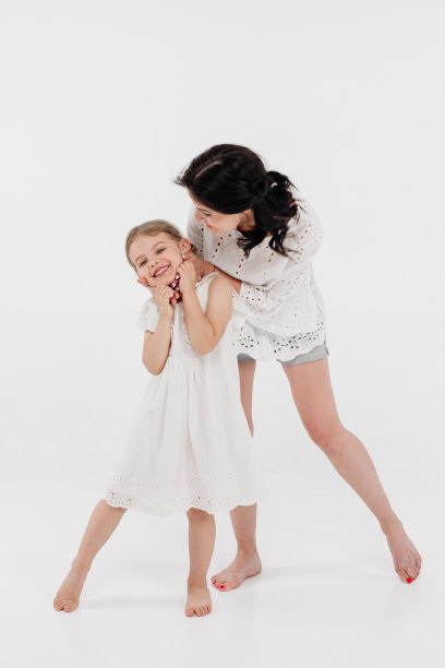 一位穿着浅色衣服的母亲正在和一个可爱的小女孩玩得很开心。母亲和小女儿被隔离在白色背景上。母亲节，爱，家庭，亲子，童年的概念。图片下载