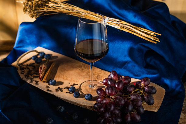 蓝缎子上的木板上的红葡萄，木制的背景点缀着灯光，一杯酒，蓝莓，肉桂，丁香和胡椒。代表着红酒的味道-库存图片图片下载