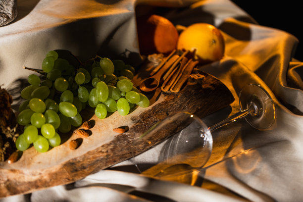 白葡萄，用木勺，肉桂，杏仁，柚子，和橙子在一块木板上的白色缎子，与空的葡萄酒杯，代表白葡萄酒的香气-库存照片图片下载