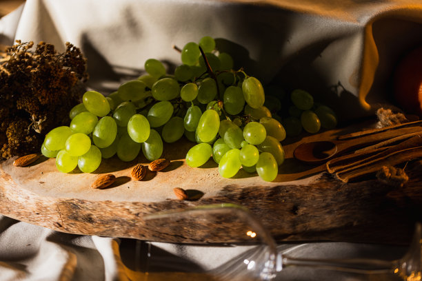 白葡萄，用木勺，肉桂，杏仁，柚子，和橙子在一块木板上的白色缎子，与空的葡萄酒杯，代表白葡萄酒的香气-库存照片图片下载