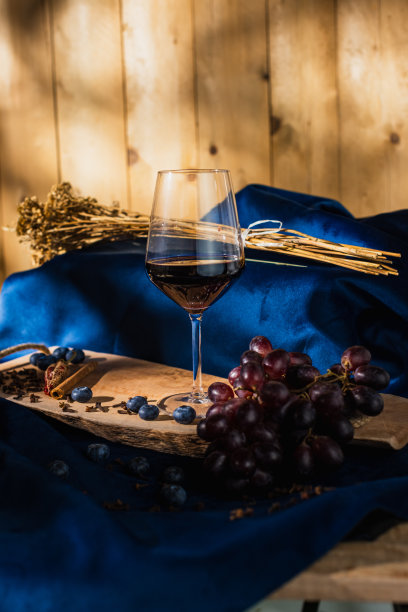 蓝缎子上的木板上的红葡萄，木制的背景点缀着灯光，一杯酒，蓝莓，肉桂，丁香和胡椒。代表着红酒的味道-库存图片图片下载
